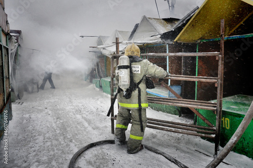 Firefighters with the inscription on the back in Russian " fire protection. Emercom of Russia" extinguish a fire on the roof of a house on a frosty winter day