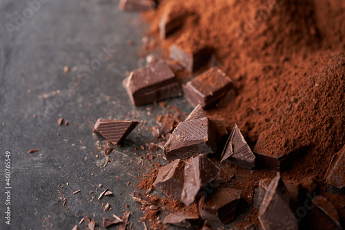Pieces of dark chocolate and heaps of cocoa powder on dark stone underground