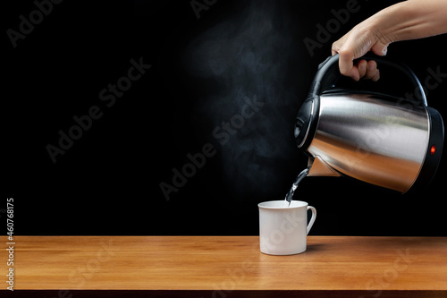 Foto pouring water from kettle water boiler into a cup with smoke on wood table and b