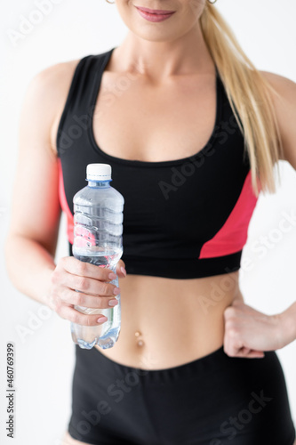 Water balance. Sportive woman. Home fitness. Healthy body. Unrecognizable athletic lady in black sportswear holding plastic bottle of clear beverage isolated white. © golubovy