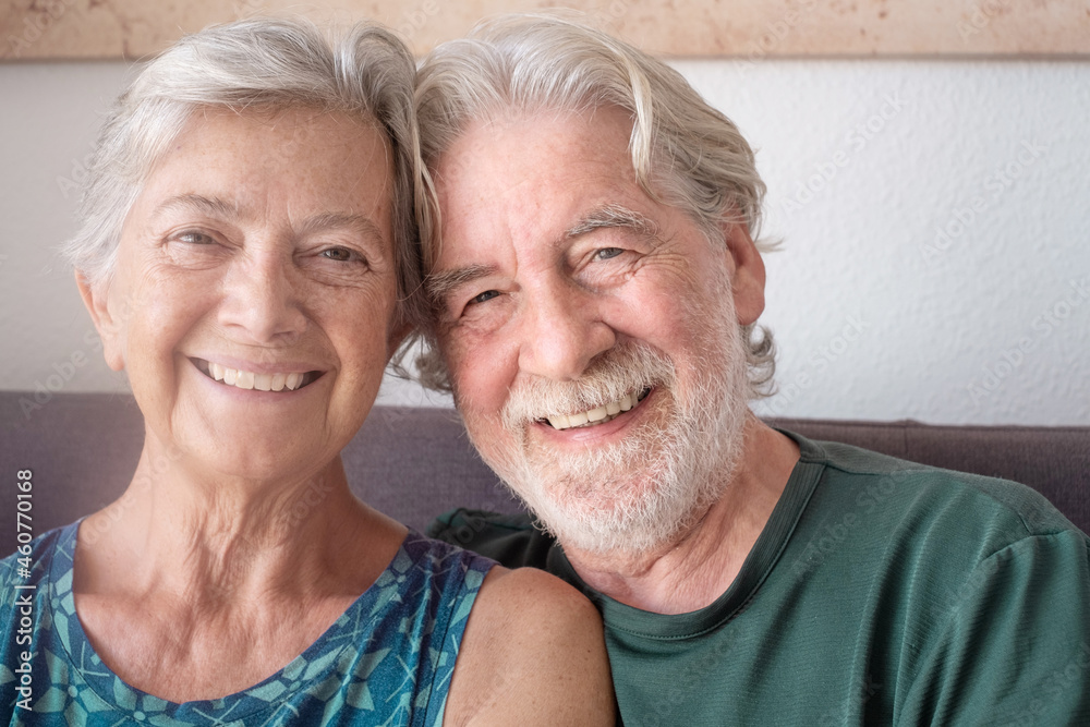 Portrait of cheerful senior couple embracing and smiling. Elderly happy couple relaxing in front of camera sitting in living room. old couple with gray hair spending leisure time together Portrait of cheerful senior couple embracing and smiling. Elderly happy couple relaxing in front of camera sitting in living room. old couple with gray hair spending leisure time together