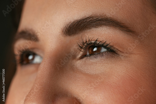 Close-up image of female brown eyes without makeup isolated over dark studio background. Natural beauty concept.