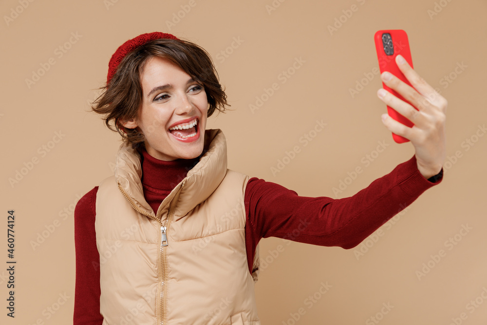 Naklejka premium Young woman 20s wears red turtleneck vest beret doing selfie shot on mobile cell phone post photo on social network isolated on plain pastel beige background studio portrait. People lifestyle concept.