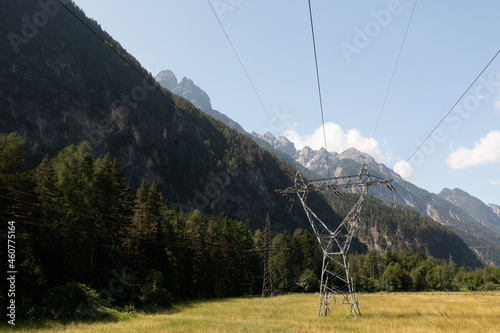 Transmission tower and power lines over the field close to the forest.