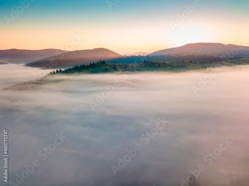 Fog spreads over the mountains at dawn. The sun rises on the horizon. Ukrainian Carpathians in the morning. Aerial drone view.