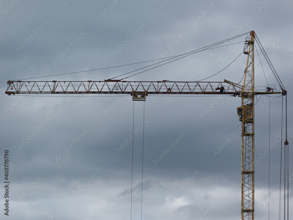 Yellow tower crane against cloudy sky background.