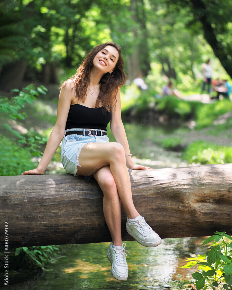 A woman in a denim skirt and a top is sitting on a log in the forest A woman in a denim skirt and a top is sitting on a log in the forest