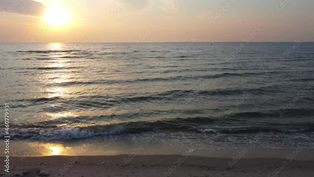 Sunrise on the sea beach. A light wind forms small waves that wash the sandy shore Sunrise on the sea beach. A light wind forms small waves that wash the sandy shore