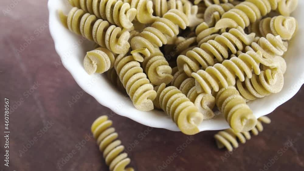 Uncooked pea fusilli pasta. Full bowl of green italian spiral vegetable macaroni on a wooden surface. Close up. Rotation Uncooked pea fusilli pasta. Full bowl of green italian spiral vegetable macaroni on a wooden surface. Close up. Rotation