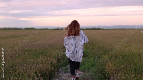 Woman in a shirt walking through a rice field while the breeze gives her.