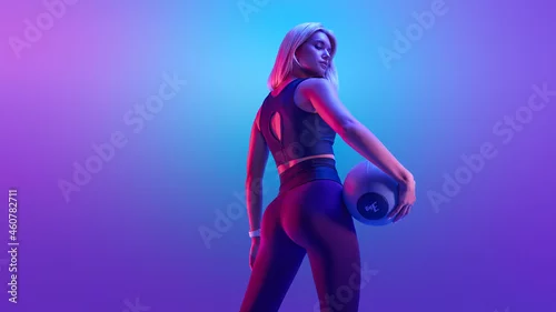 Obraz Confident fitness woman posing with a medicine ball. Attractive blonde sportswoman portrait holding with medicine fitness ball neon style creative light.