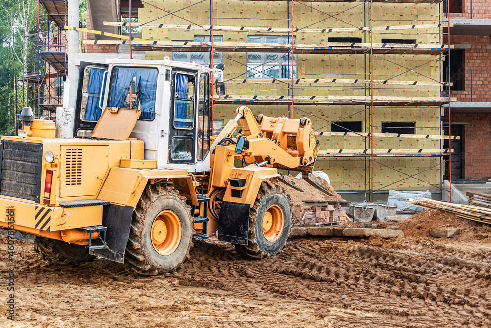 A forklift at a construction site is lifting a reinforced concrete slab. Construction machine. Construction of a brick building and thermal insulation with mineral wool. A forklift at a construction site is lifting a reinforced concrete slab. Construction machine. Construction of a brick building and thermal insulation with mineral wool.