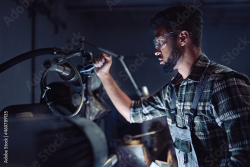 Portrait of young concentrated african american industrial man working on cutter indoors in metal workshop.