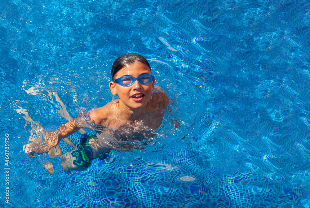 Portrait of a smiling boy in the outdoor pool. Teenager in swimming goggles. Summer vacation at the hotel or outdoor swimming lessons. Healthy lifestyle concept