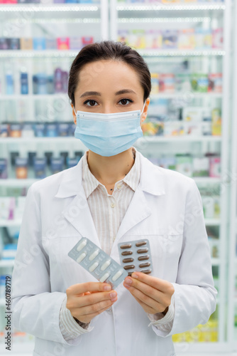 Obraz na plátně apothecary in medical mask holding blister packs with medication