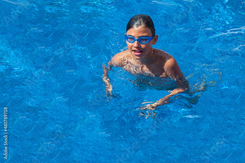 Portrait of a smiling boy in the outdoor pool. Teenager in swimming goggles. Summer vacation at the hotel or outdoor swimming lessons. Healthy lifestyle concept