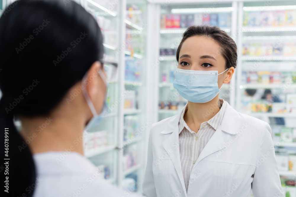 tattooed pharmacist in medical mask looking at blurred colleague tattooed pharmacist in medical mask looking at blurred colleague