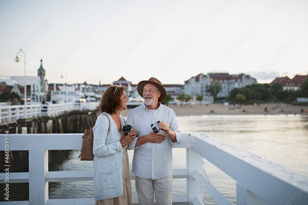 Happy senior couple tourist having fun on walk outdoors on pier by sea, summer holiday.