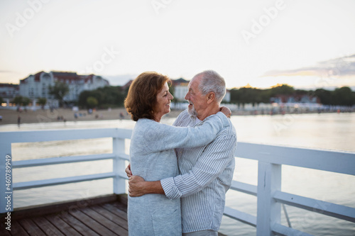 Happy senior couple in love hugging outdoors on pier by sea, looking at each other.