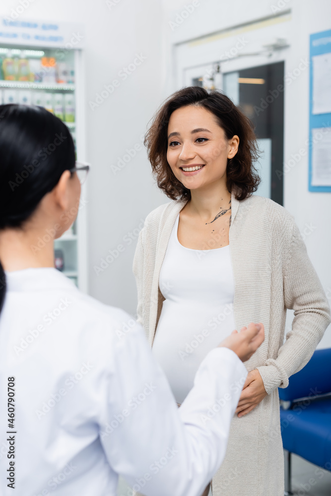 pregnant woman with tattoo smiling while looking at blurred pharmacist in drugstore pregnant woman with tattoo smiling while looking at blurred pharmacist in drugstore