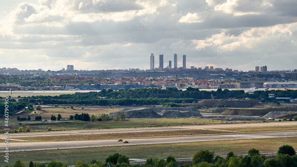 Runway at Madrid Barajas airport with airport services cars circulating on it with views of the city and its famous office towers behind