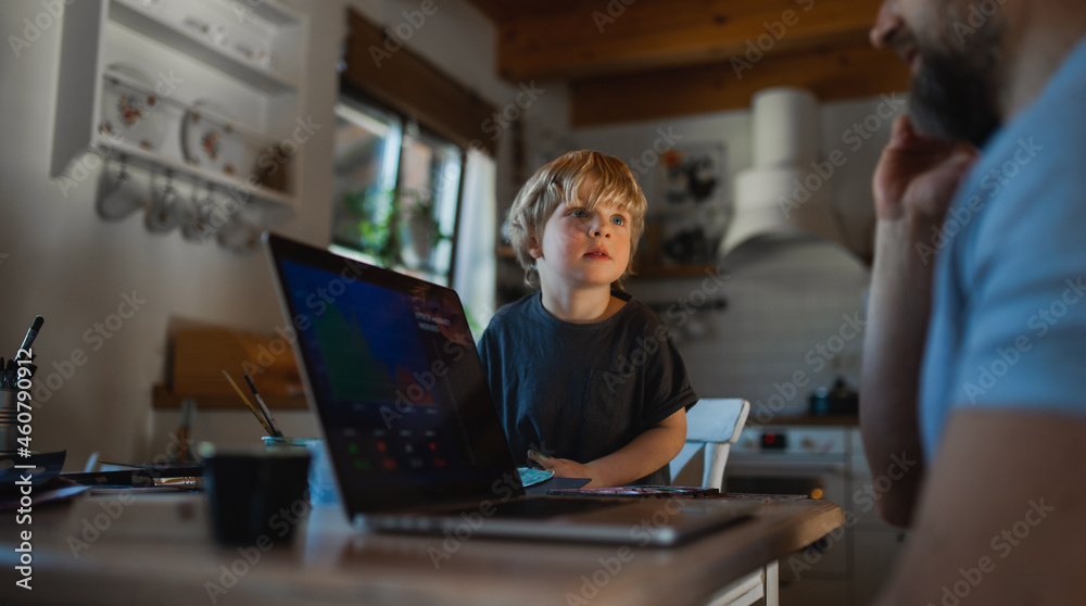 Unrecognizable father with small son working indoors at home, painting pictures and home office concept. Unrecognizable father with small son working indoors at home, painting pictures and home office concept.