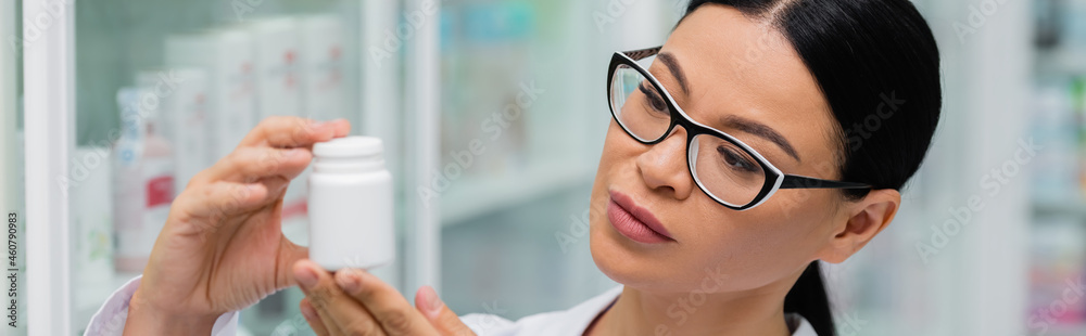 brunette asian pharmacist in glasses holding bottle with medication, banner brunette asian pharmacist in glasses holding bottle with medication, banner