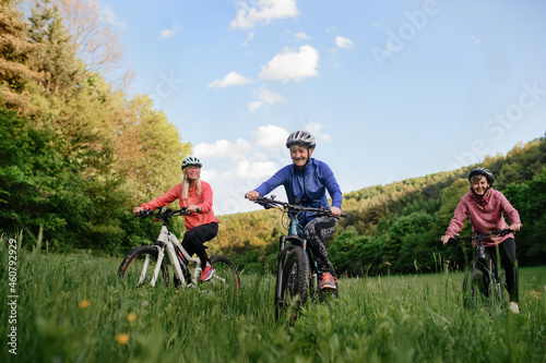 Low angle view of happy active senior women friends cycling together outdoors in nature.