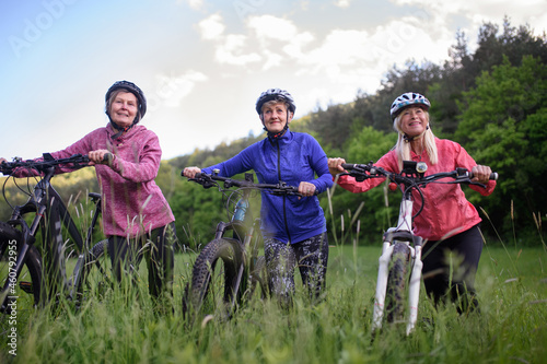 Low angle view of happy active senior women friends pushing bicycles together outdoors in nature.