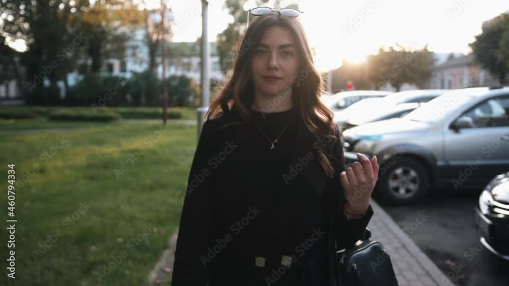 A spectacular young girl in a stylish black outfit and with sunglasses on her head goes along a city street at sunset A spectacular young girl in a stylish black outfit and with sunglasses on her head goes along a city street at sunset