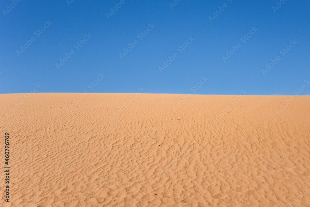 Naklejka premium Ripple sand dunes and blue sky background. Desert landscape, sandy waves. Nature.