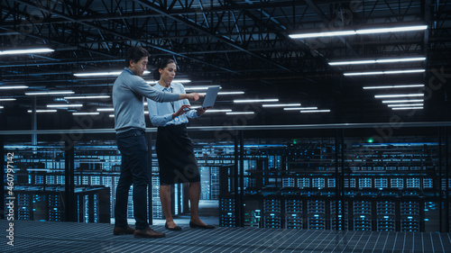 Data Center Female System Administrator and Male IT Specialist Talk, Use Laptop Computer. Information Technology Engineers work on Cyber Security Network Protection in Cloud Computing Server Farm.