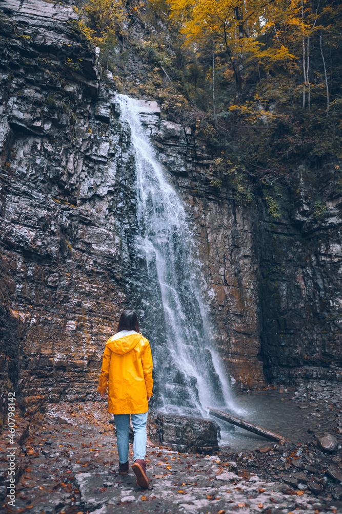 Obraz premium woman in yellow raincoat at autumn waterfall