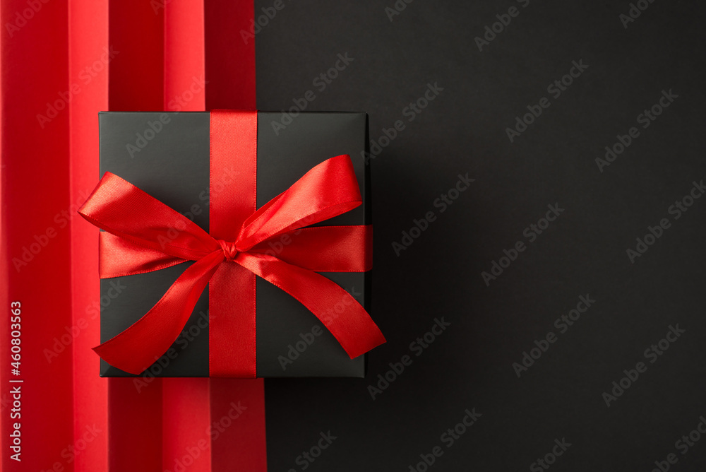 Top view photo of black giftbox with red ribbon bow and red sheet with vertical folds on isolated black background with empty space