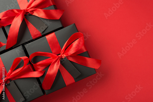 Top view photo of black gift boxes with red ribbon bow and tags on isolated red background with blank space