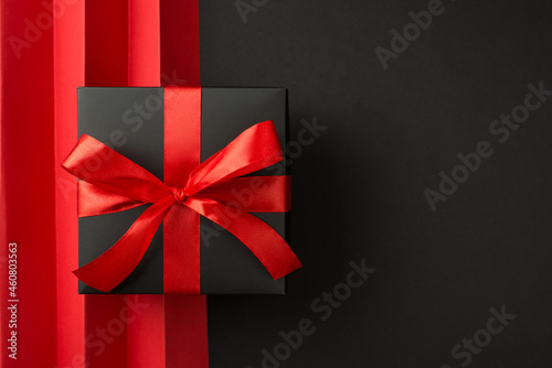 Top view photo of black giftbox with red ribbon bow and red sheet with vertical folds on isolated black background with empty space