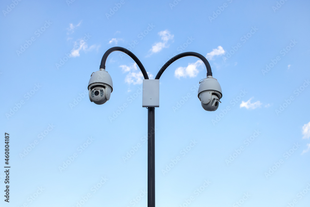 Surveillance cctv (closed circuit television) camera installed in public park on blue sky background for protection against crime, observation of people, control of observance of public order Surveillance cctv (closed circuit television) camera installed in public park on blue sky background for protection against crime, observation of people, control of observance of public order
