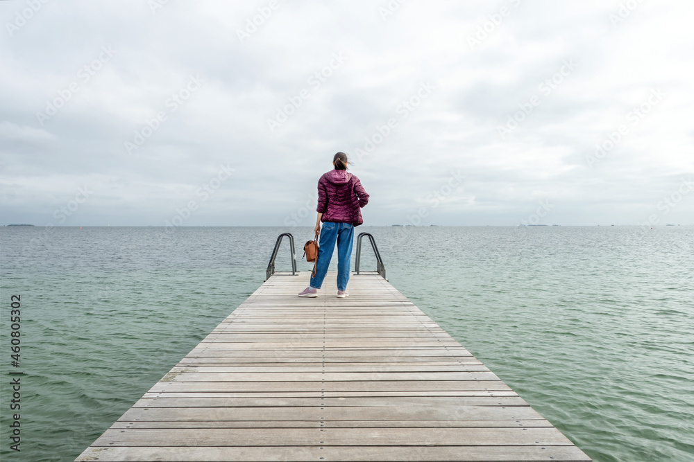 Young girl with a backpack, looks at the sea, on a wooden pier. Freedom. Trips.
