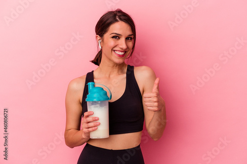 Young caucasian woman drinking a protein shake isolated on pink background