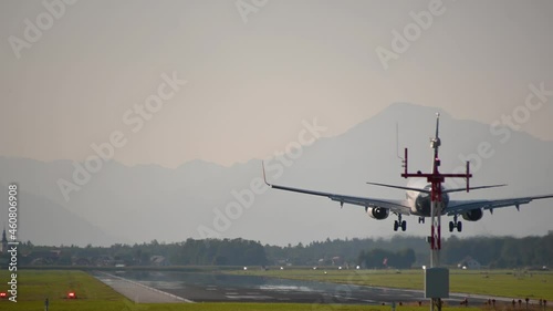 Large passenger plane landing at international Ljubljana Airport, Slovenia. Airplane touchdown. Aircraft on long runway, rear view. Air travel concept. Static shot, real time, telephoto perspective