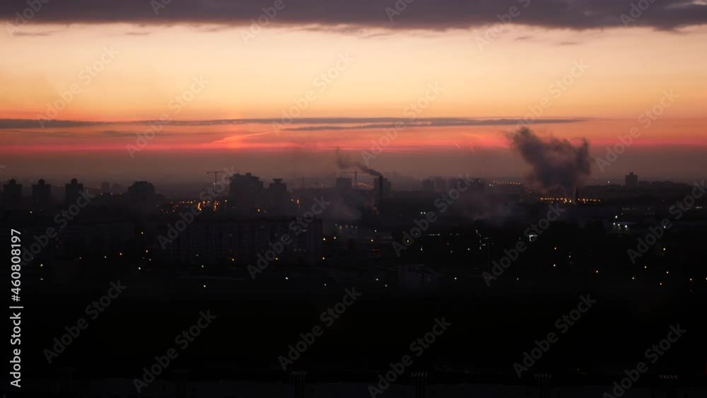 Cityscape with smoking stacks, silhouettes of lifting cranes and buildings on the background of sunrise. Smoke issues from the factory chimneys in the early morning. City awakens Cityscape with smoking stacks, silhouettes of lifting cranes and buildings on the background of sunrise. Smoke issues from the factory chimneys in the early morning. City awakens