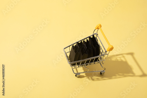 Miniature supermarket cart with shopping bags in black friday sale on yellow background