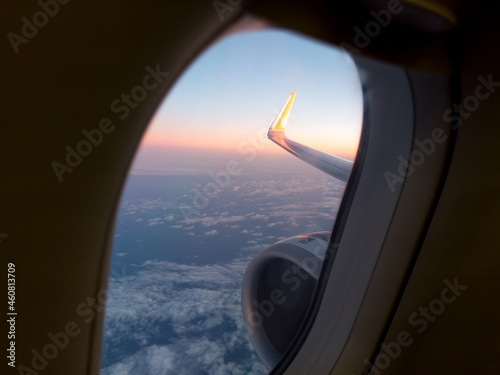 Blue sky and white clouds view from porthole airplane at sunrise dawn. clouds under airplane wing with engine