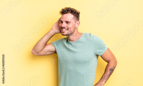 young handsome hispanic man smiling, looking curiously to the side, trying to listen to gossip or overhearing a secret photo