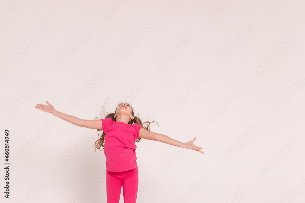 a beautiful girl in a pink jumps and smiles on a white background. happy childhood.