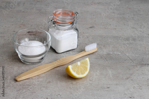 Baking soda in a glass jar, lemon and bamboo toothbrush on a gray concrete background with copy space. Natural teeth whitening at home.  photo