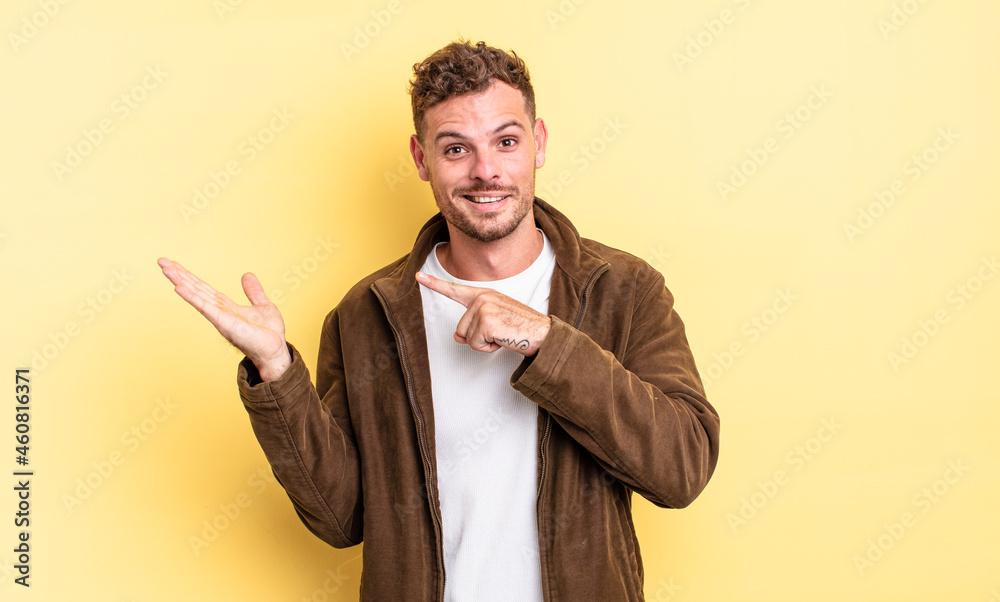Obraz premium young handsome hispanic man smiling cheerfully and pointing to copy space on palm on the side, showing or advertising an object