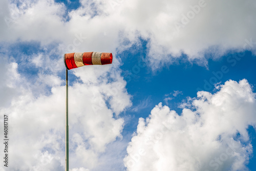Red and white checkered windsock against a cloudy sky. The windsock is mounted on a steel pole. The photo was taken on a windy day in the Netherlands.