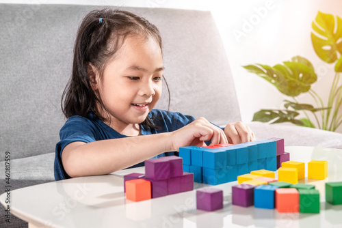 Asian girl plays with small wooden colorful toy blocks at home or kindergarten. A Girl enjoys playing with construction blocks for toddler kids. Education Development Construction creative toys Idea