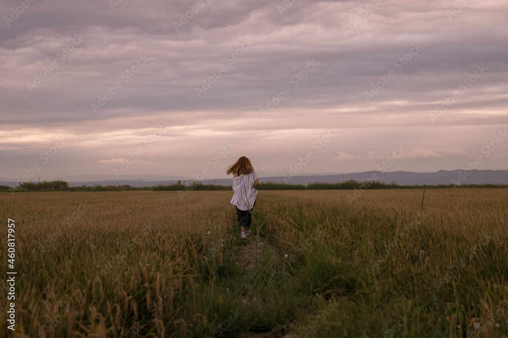 Woman in a shirt walking through a rice paddy at sunset